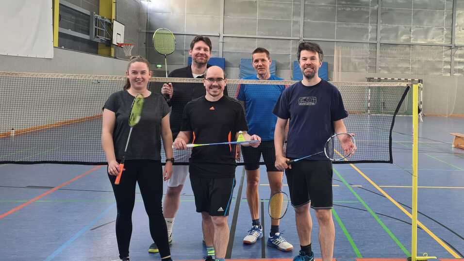 Teammitglieder von Sportgruppe 61 stehen für ein Gruppenbild in Trainingsklamotten vor einem Badminton-Netz